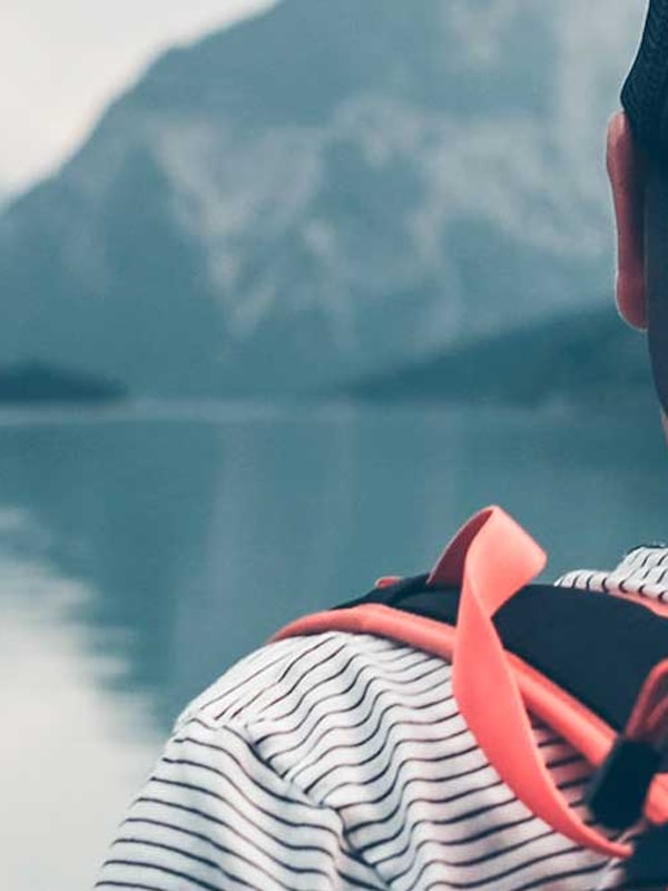 Person med sort caps og ryggsekk ser ut over fjord mellom høye fjell